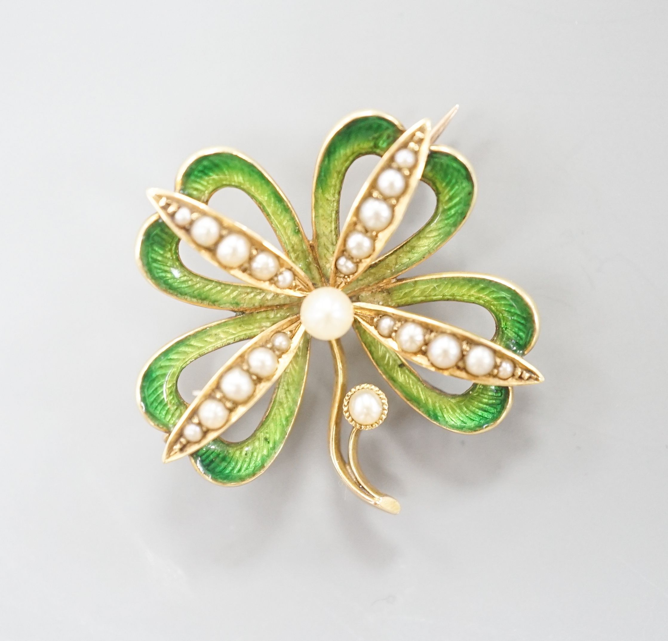 An Edwardian 15ct, seed pearl and green enamel set clover brooch, with later bale attachment, width 24mm, gross weight 4.4 grams.